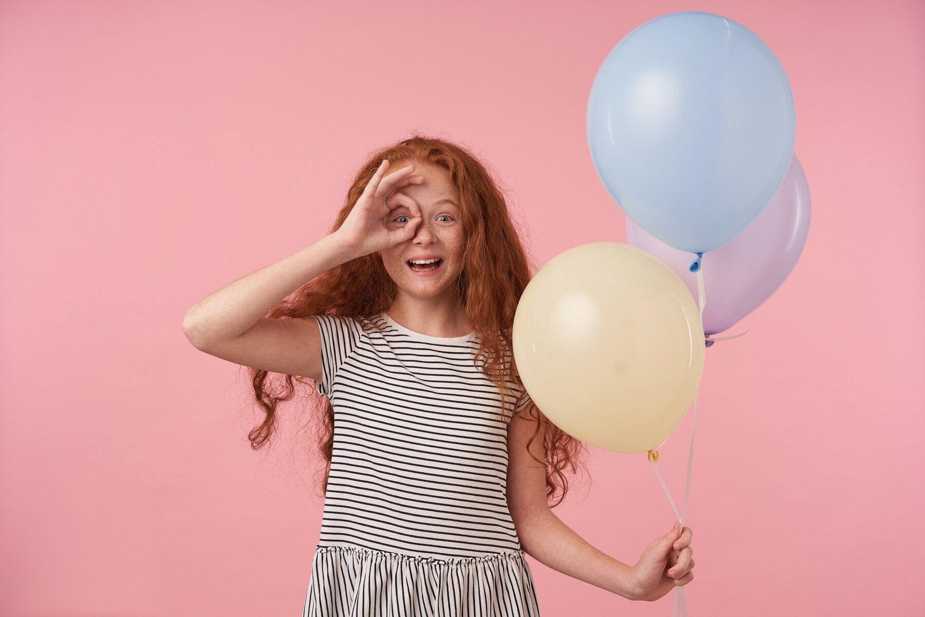 happy-cute-redhead-curly-female-kid-raising-hand-with-ok-gesture-her-eye-posing-pink-background-with-air-ballons-looking-camera-joyfully-smiling-widely_295783-6973.jpeg